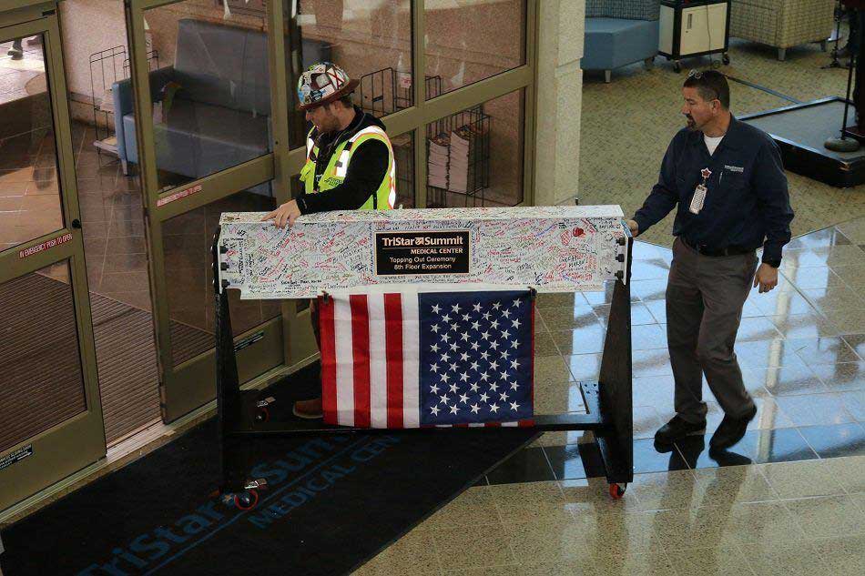 Two workers roll out the final steel beam, which is white and covered in staff signatures